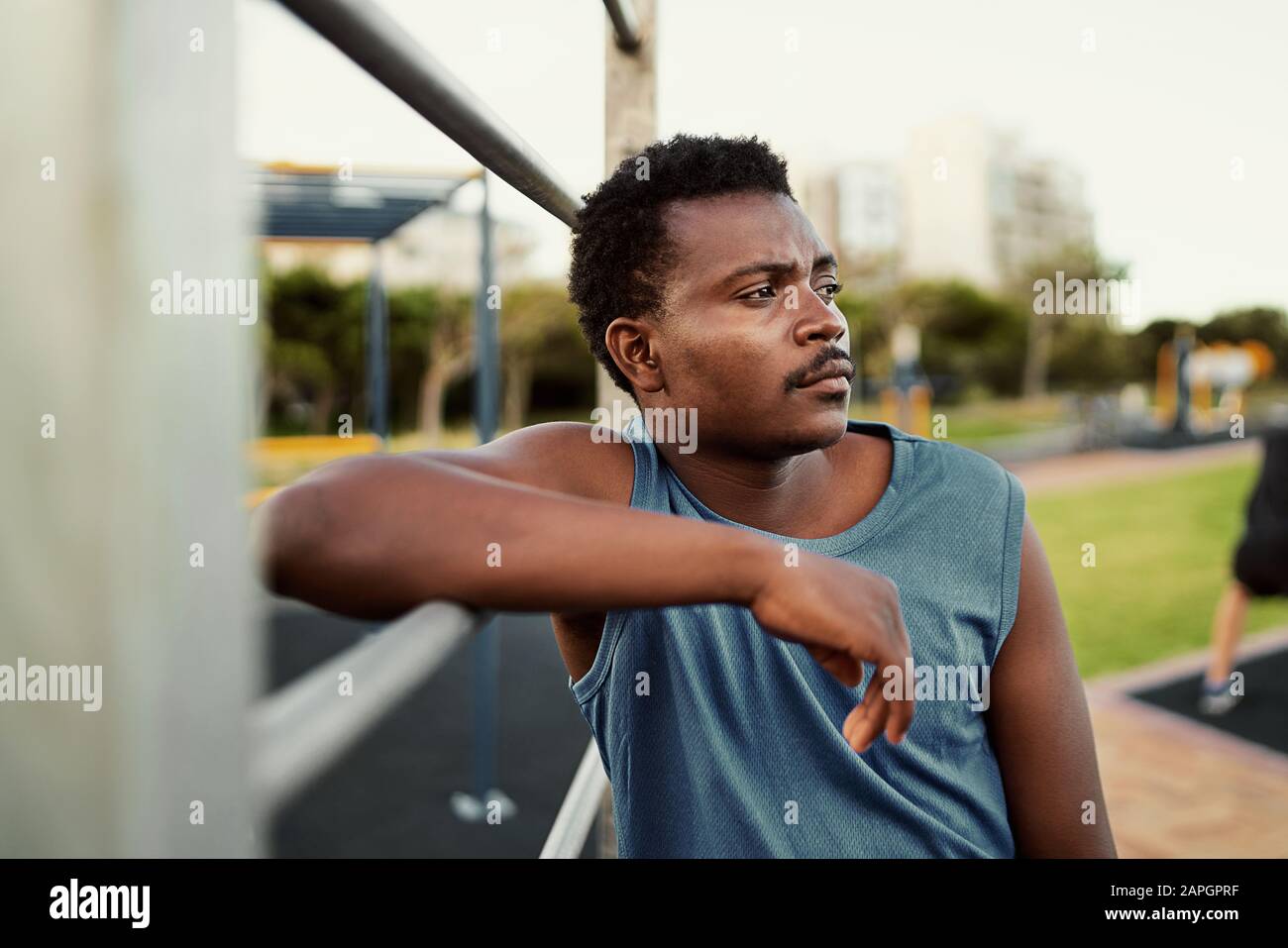 Portrait eines erwogenen jungen Fitness-Gesellen, der sich an der Griffstange anlehnt, nachdem er im öffentlichen Park-Fitnessstudio trainiert hat Stockfoto