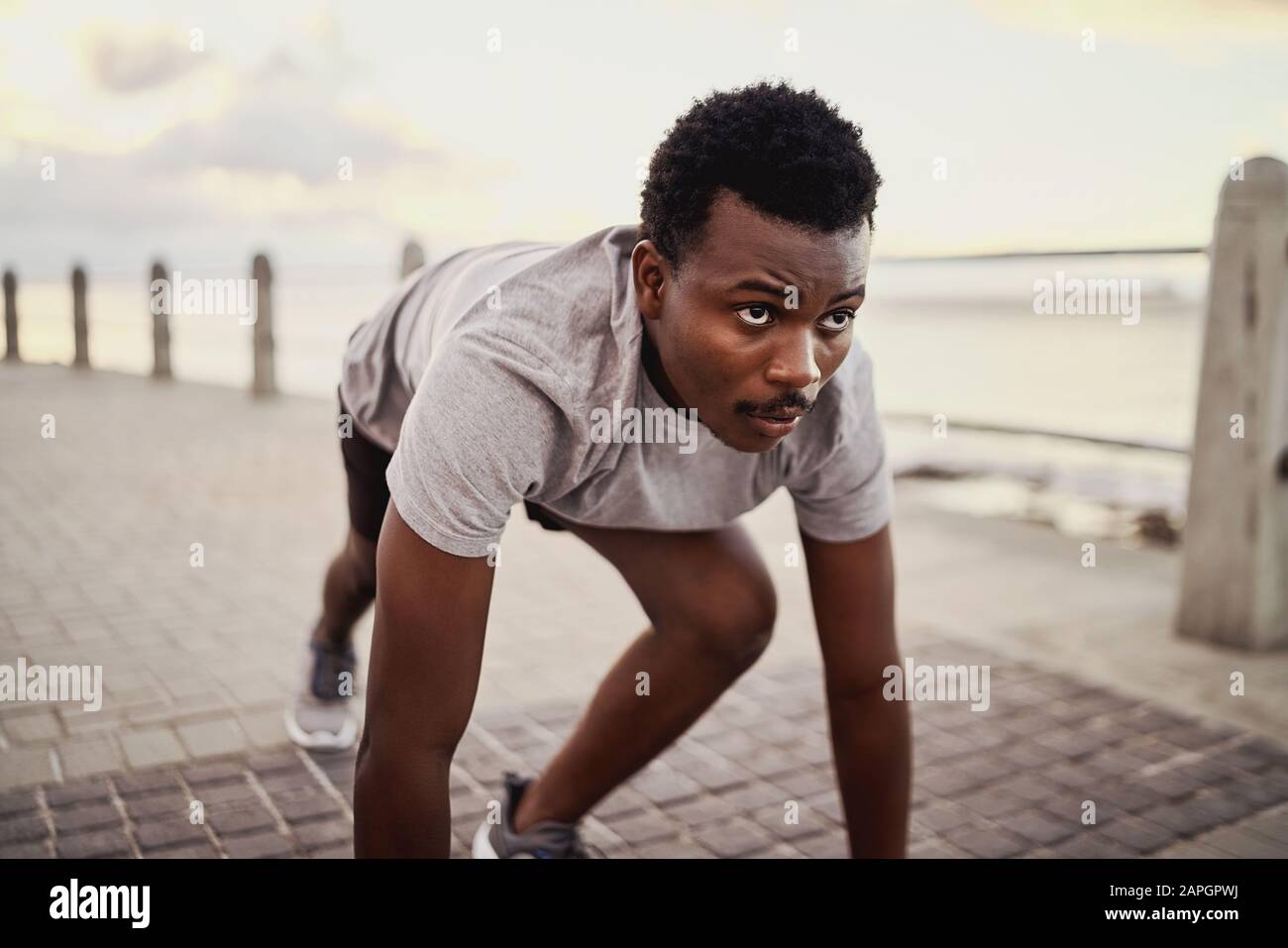Portrait eines jungen afroamerikanischen männlichen Athleten in der Startposition, der sich auf das laufen auf dem Meer vorbereitet Stockfoto