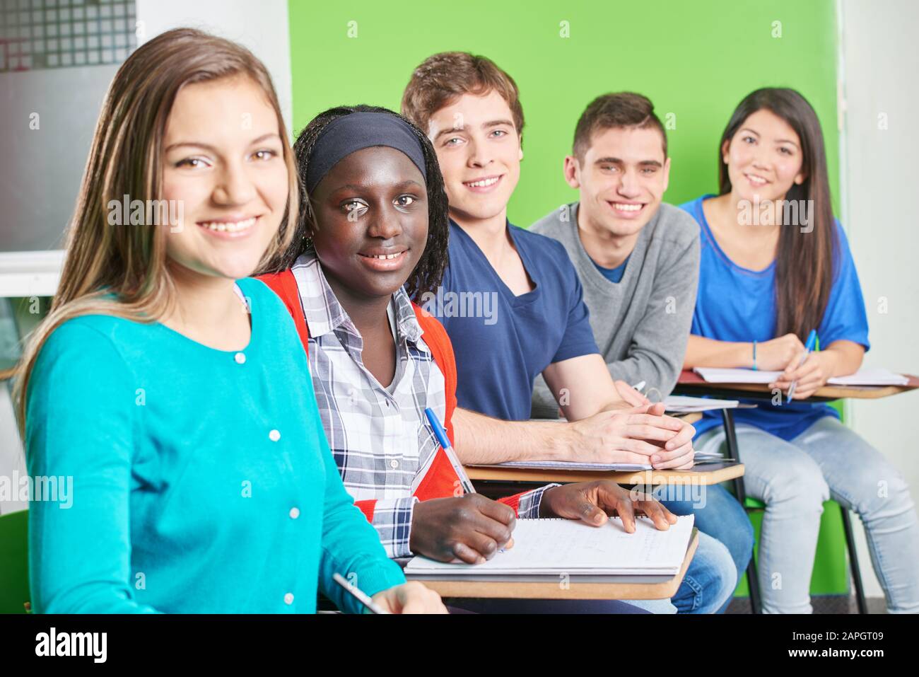 Multikulturelle Gruppe von Schülern, die lächelnd in der Schule sitzen Stockfoto