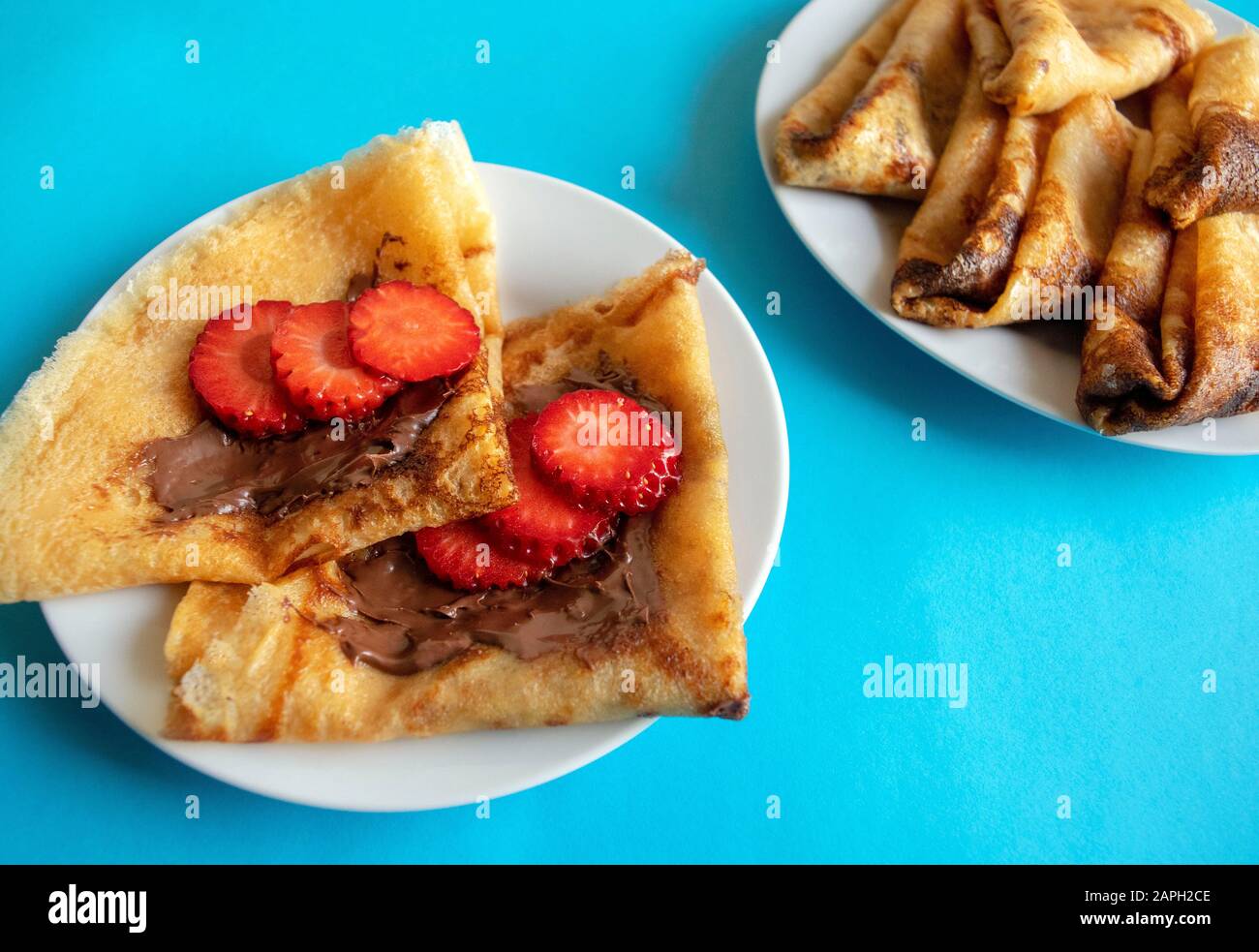 Frische Pfannkuchen mit Schokoladenpaste und Erdbeere auf blauem hellem Hintergrund. Pfannkuchen im russischen Stil für Die Pancake-Woche. Pfannkuchen in englischer Fassung. Stockfoto
