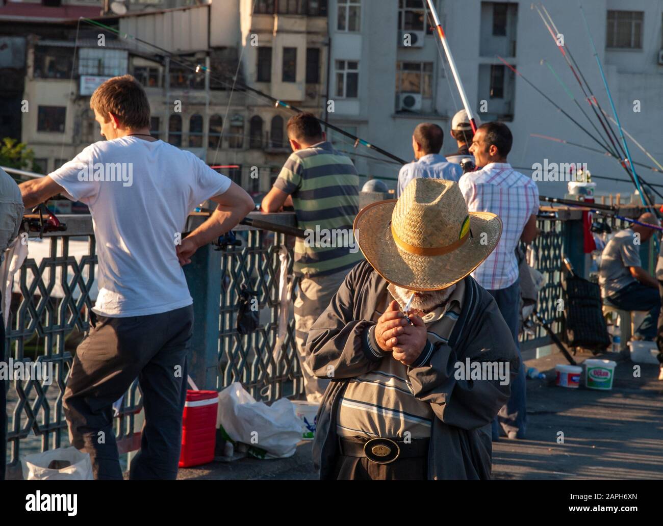 Istanbul/Türkei alter Mann mit Strohhut beleuchtet eine Zigarette auf der Galata-Brücke. Mehrere Fischer im Hintergrund. Stockfoto