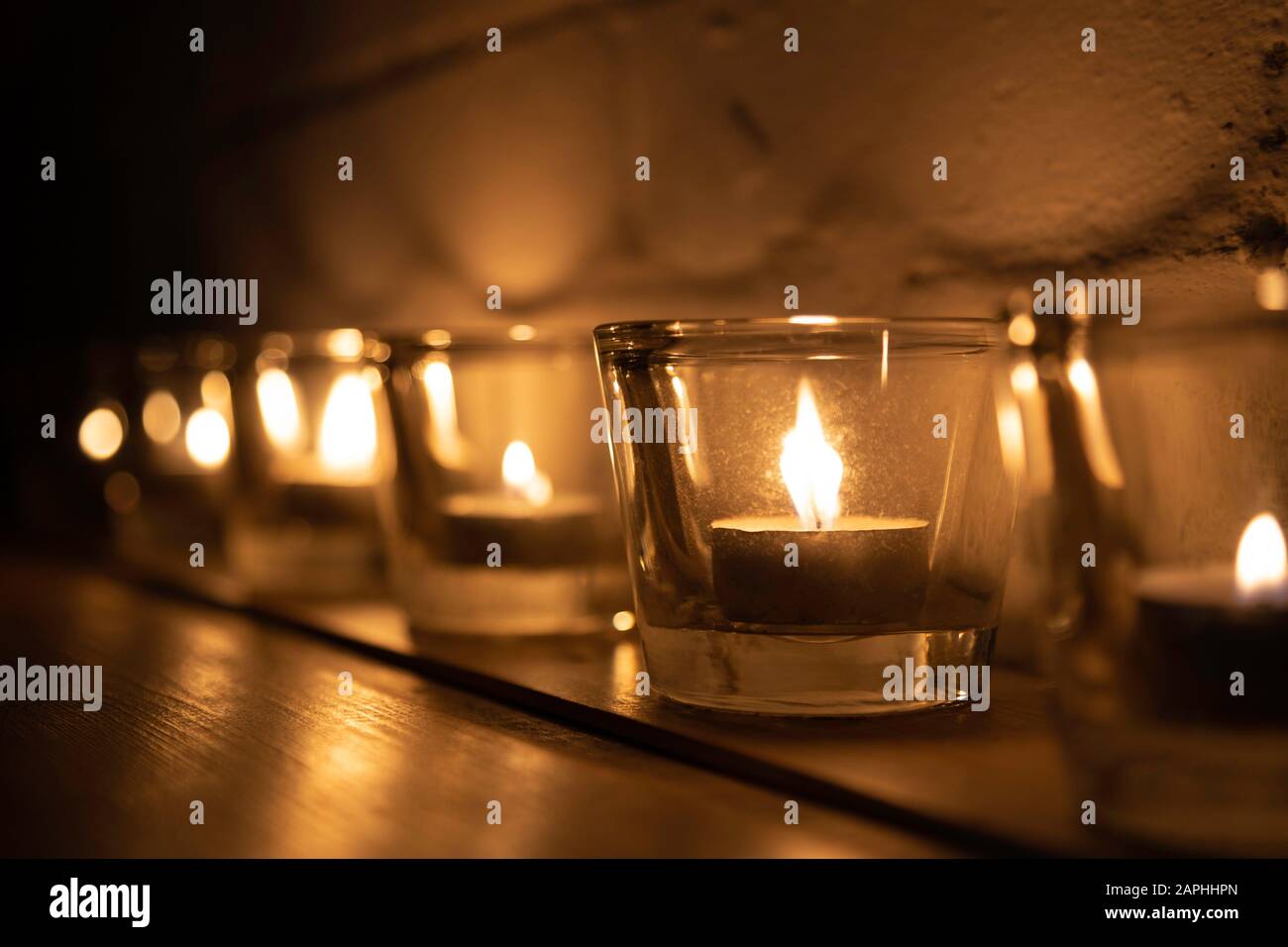 Reihe von Votivkerzen und Teeleuchten in einer Reihe mit Kerzenlicht Stockfoto