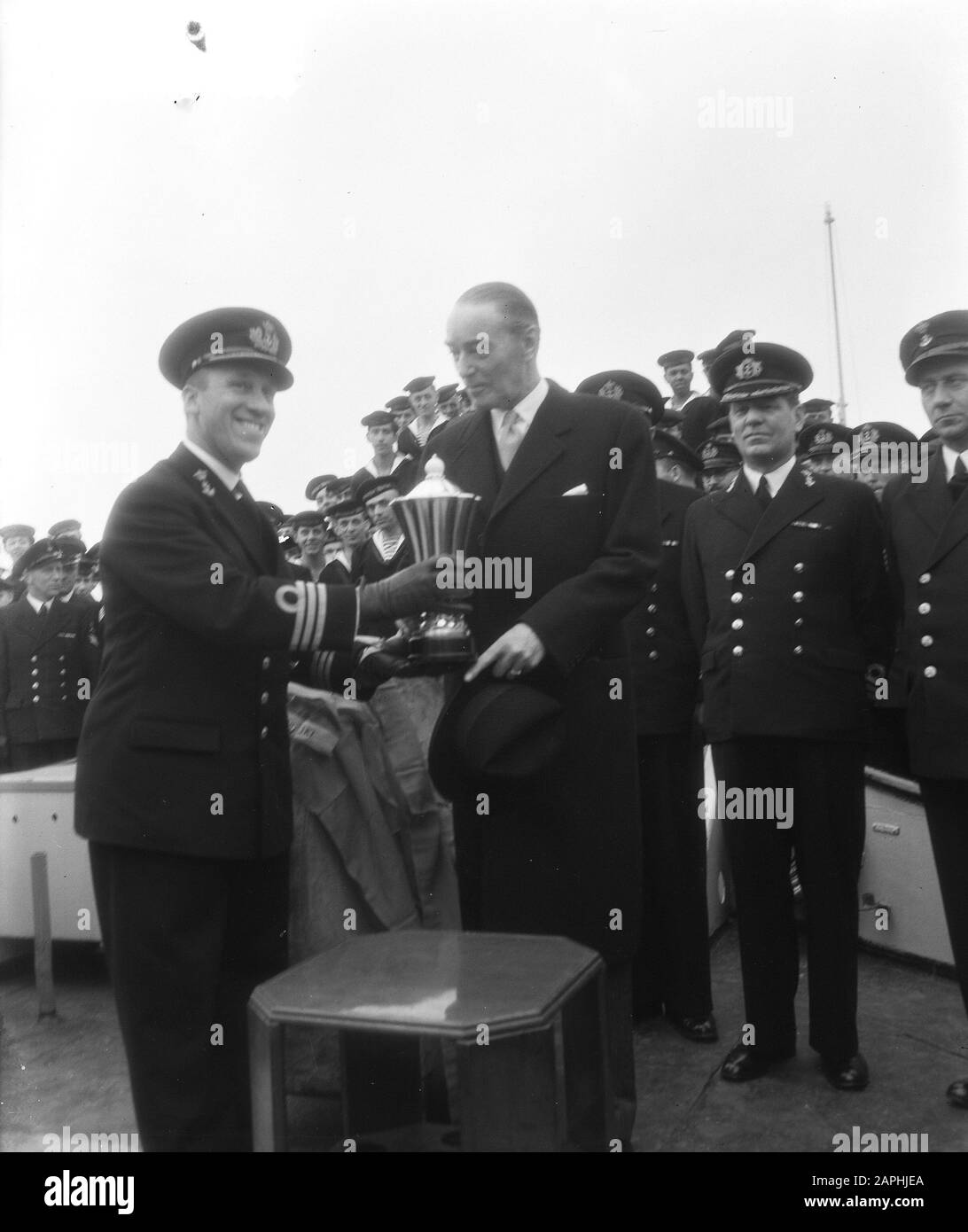 Geschenkbecher an den Kommandanten von H.M. Evertsen durch den dänischen Gesandten in Rotterdam Beschreibung: Der Kommandant erhält den Becher aus den Händen des Gesandten Anmerkung: Der Kelch wurde vom dänischen Gesandten J.W.H. Eickhof als Dankeschön für die Hilfe, die die Evertsen dem dänischen Motorradschoner Svaerdfisken angeboten hatten Datum: 4. april 1955 Ort: Rotterdam, Zuid-Holland Schlagwörter: Cup Awards, Kommandeure, Naval Personname: EVERTSEN HR. MS. Stockfoto