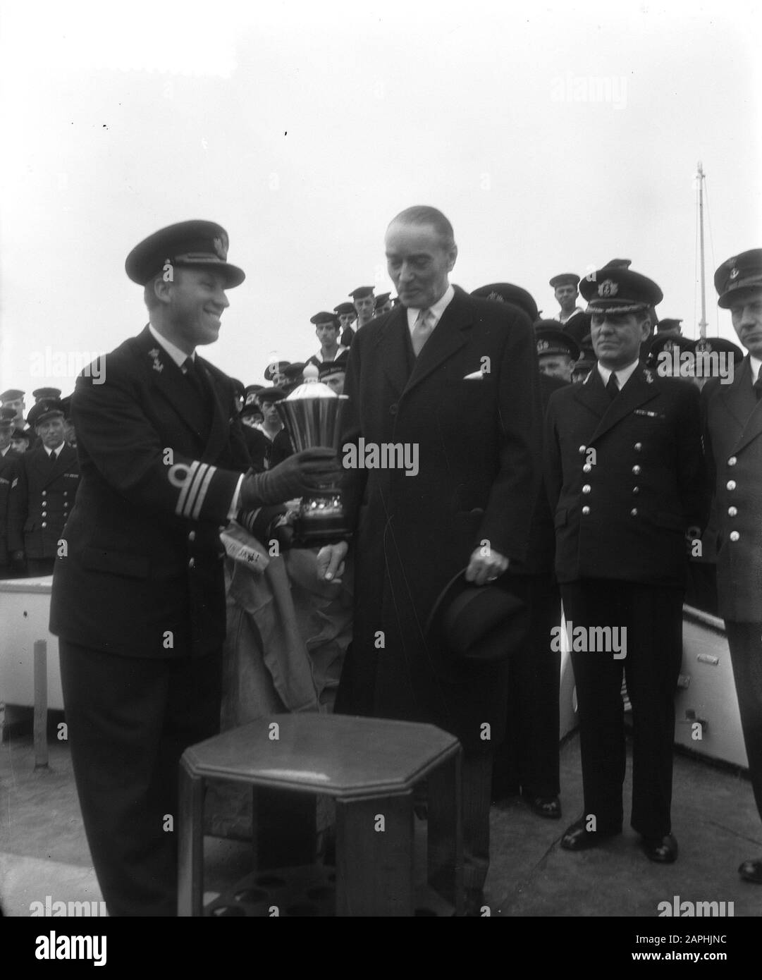 Geschenkbecher an den Kommandanten von H.M. Evertsen durch den dänischen Gesandten in Rotterdam Beschreibung: Der Kommandant erhält den Becher aus den Händen des Gesandten Anmerkung: Der Kelch wurde vom dänischen Gesandten J.W.H. Eickhof als Dankeschön für die Hilfe, die die Evertsen dem dänischen Motorradschoner Svaerdfisken angeboten hatten Datum: 4. april 1955 Ort: Rotterdam, Zuid-Holland Schlagwörter: Cup Auszeichnungen, Kommandeure, Marine Stockfoto