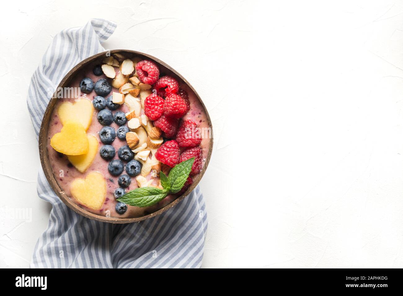 Banane und Blaubeere Smoothie auf Weiß. Gesundes Frühstück in der Kokosschale. Ansicht von oben mit Kopierbereich. Sauberes Essen, vegetarisches Essen. Stockfoto