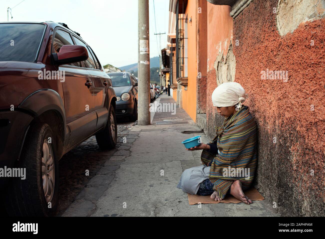 Indigene guatemaltekische Frau bettelt auf der Straße in der Nähe eines Luxuswagens. Ungleichheit in Antigua, Guatemala. Januar 2019 Stockfoto