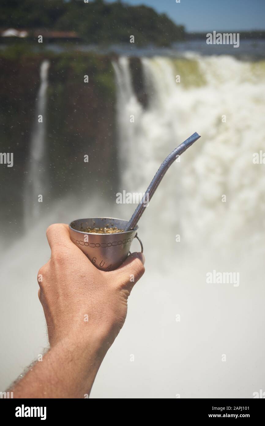 Hand, die Tereré Cup vor den Iguazu Falls hält Stockfoto