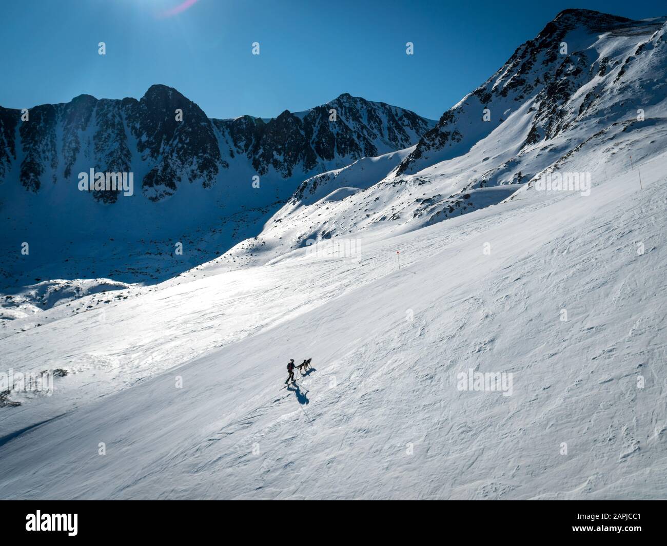 Silhouette einer Frau mit ihrem Hund, der Skibergsteigen macht, und einem atemberaubenden Blick auf die Schnee-Berge Stockfoto