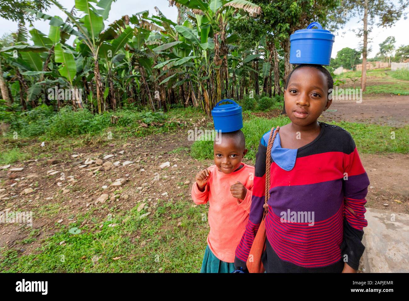 Kinder, die ihre Lebensmittelbehälter auf dem Kopf tragen, in Kitwa, Uganda Stockfoto