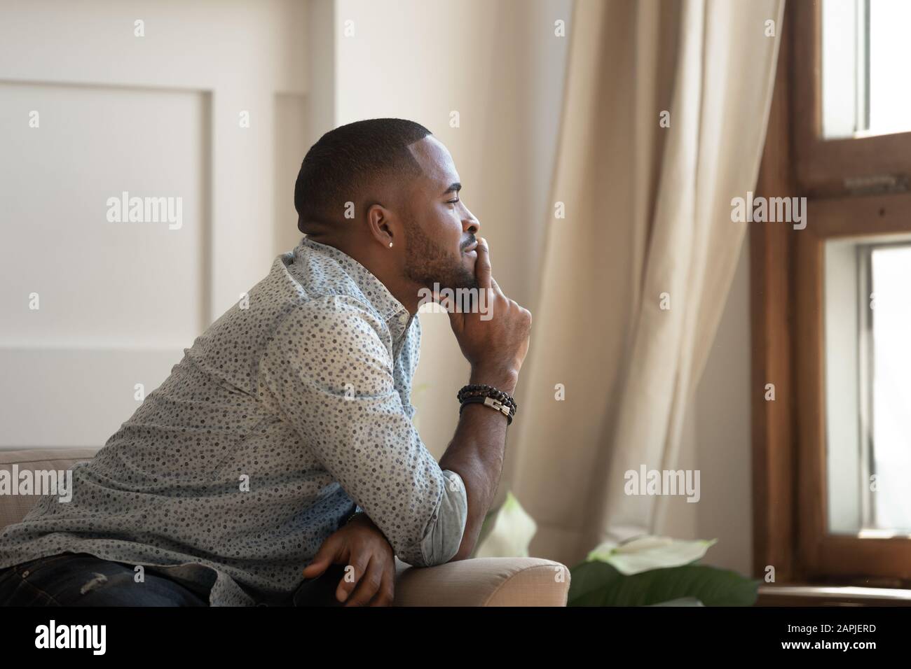 Penibler afrikanischer Mann, der auf der Couch sitzt und aus dem Fenster blickt Stockfoto
