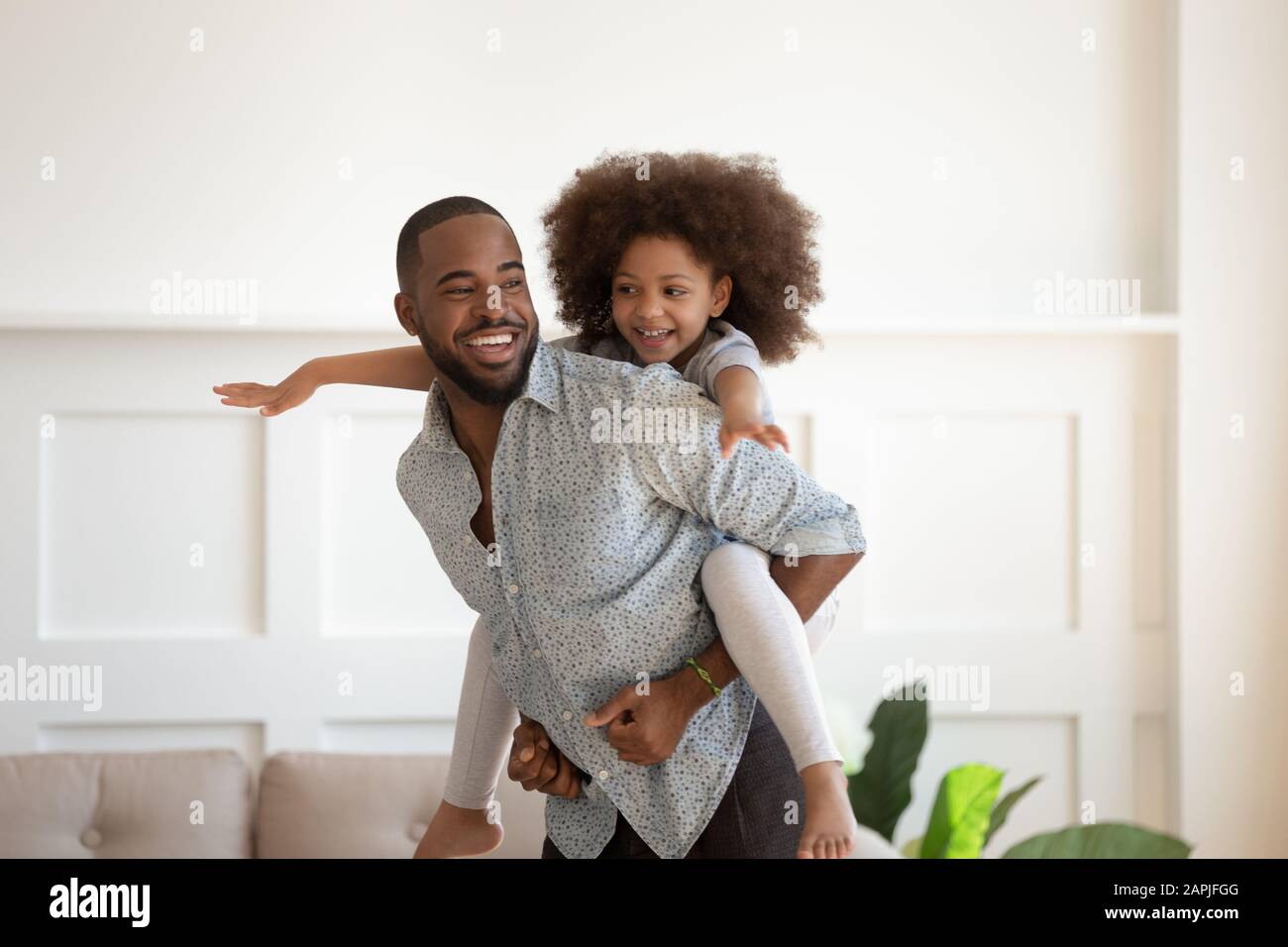 Fröhlicher afrikanischer Vater piggybacking kleine Tochter, die zusammen drinnen spielt Stockfoto