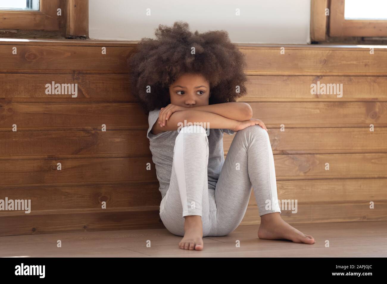 Trauriges, kleines afrikanisches Mädchen, das auf dem Boden sitzt, fühlt sich einsam an Stockfoto