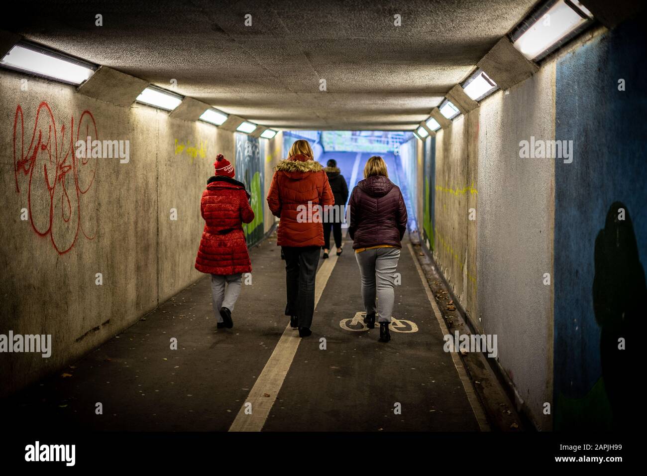 Drei Frauen in Winterkleidung, die nebeneinander unter einer Unterführung oder einer Fußgänger-U-Bahn spazieren gehen Stockfoto