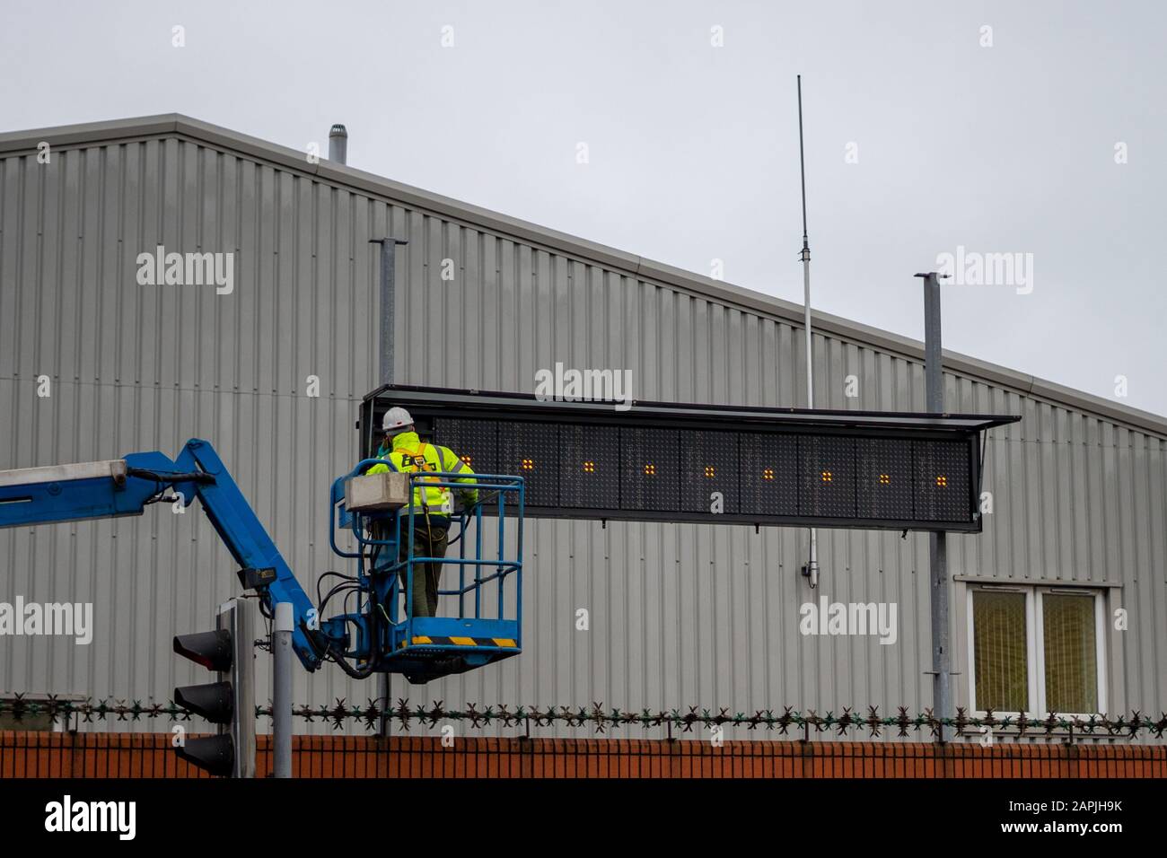 Ein Wartungstechnikarbeiter in gut sichtbarer Kleidung und ein Harthut, der an der Befestigung eines Schilderbretts auf einem Kirschpflücker arbeitet Stockfoto