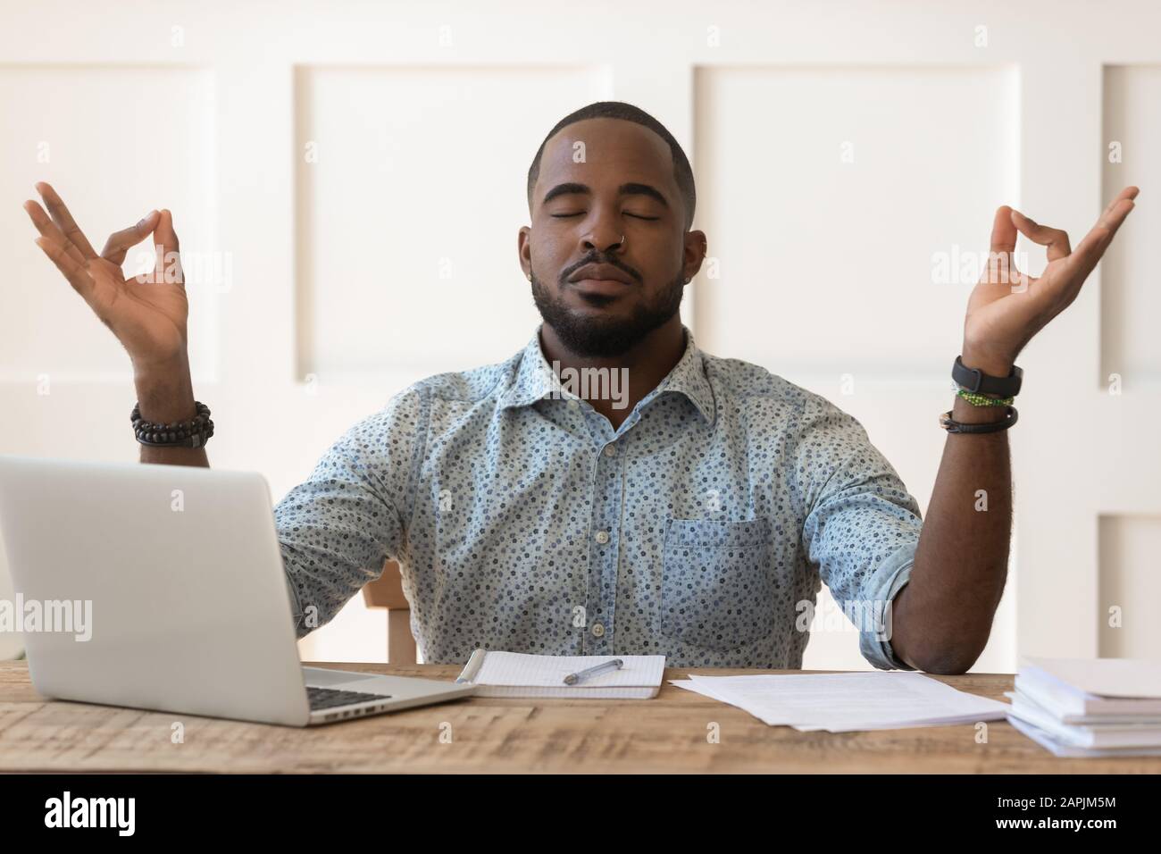 Afrikanischer Mann sitzt am Schreibtisch und meditiert während des Arbeitstages am Arbeitsplatz Stockfoto