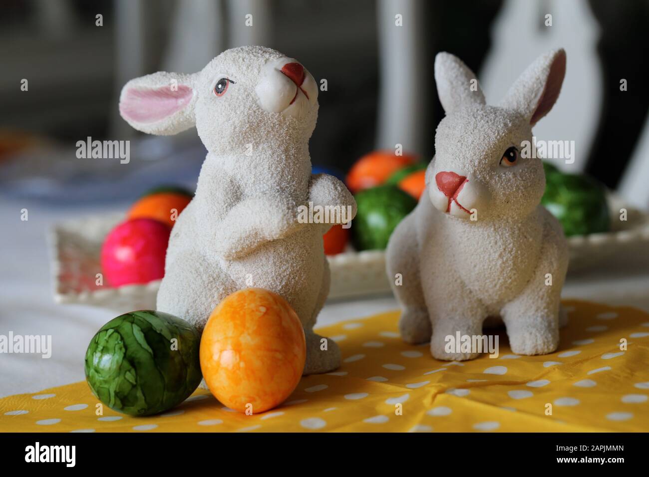 Bunte und fröhliche Osterdekorationen auf einem Tisch. Nahfarbenbild von zwei keramischen Osterhasen und bunt bemalten Ostereiern. Stockfoto