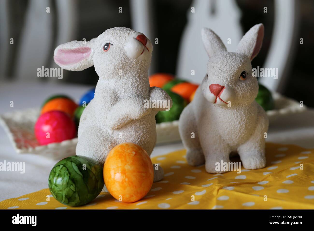 Bunte und fröhliche Osterdekorationen auf einem Tisch. Nahfarbenbild von zwei keramischen Osterhasen und bunt bemalten Ostereiern. Stockfoto