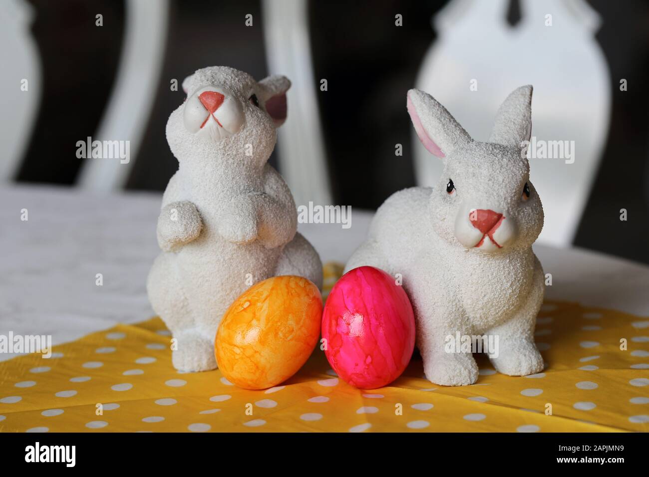 Bunte und fröhliche Osterdekorationen auf einem Tisch. Nahfarbenbild von zwei keramischen Osterhasen und bunt bemalten Ostereiern. Stockfoto