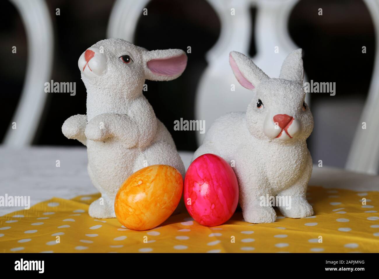 Bunte und fröhliche Osterdekorationen auf einem Tisch. Nahfarbenbild von zwei keramischen Osterhasen und bunt bemalten Ostereiern. Stockfoto