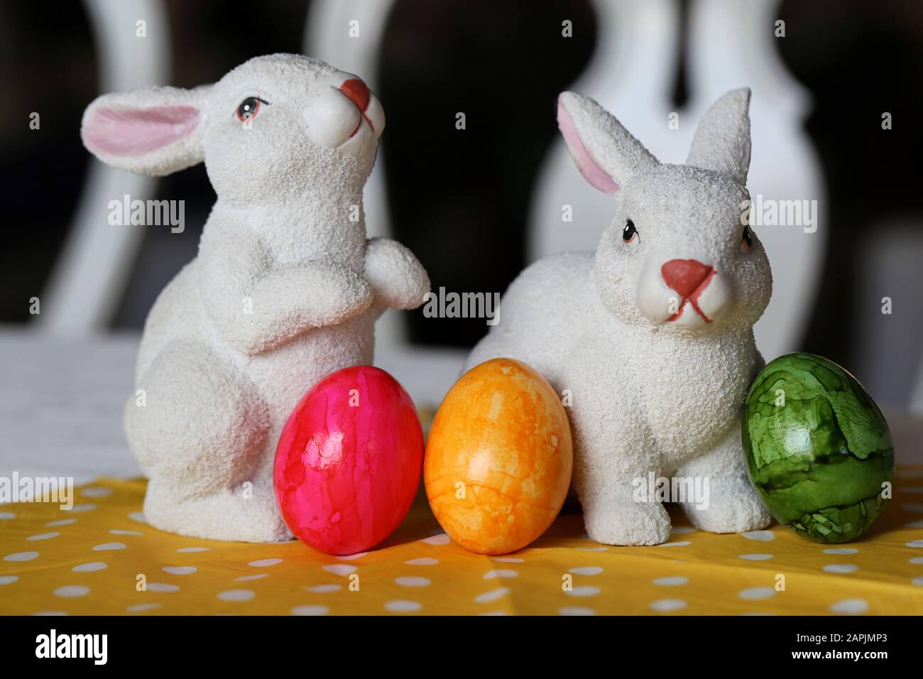 Bunte und fröhliche Osterdekorationen auf einem Tisch. Nahfarbenbild von zwei keramischen Osterhasen und bunt bemalten Ostereiern. Stockfoto