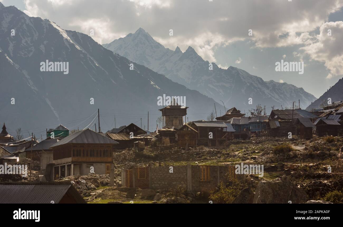 Der alte Holztempel und die Häuser des Dorfes Chitkul liegen vor dem Hintergrund der hohen schneebedeckten Berge des Himalayas, die sie umgeben Stockfoto