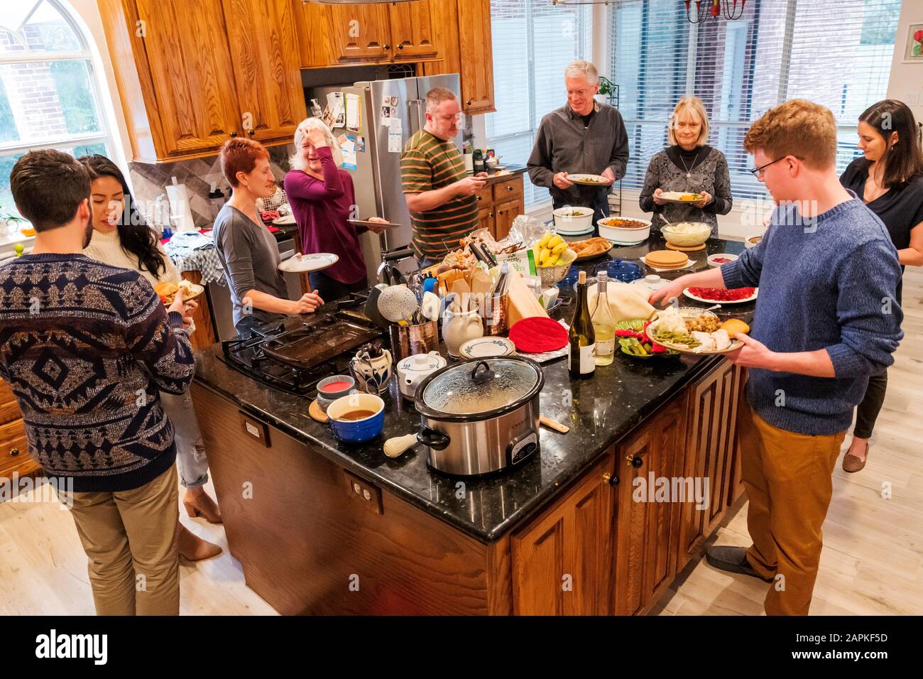 Die Familie versammelte sich um die Insel im Küchenzentrum zum Abendessen am Thanksgiving in Buffetform Stockfoto