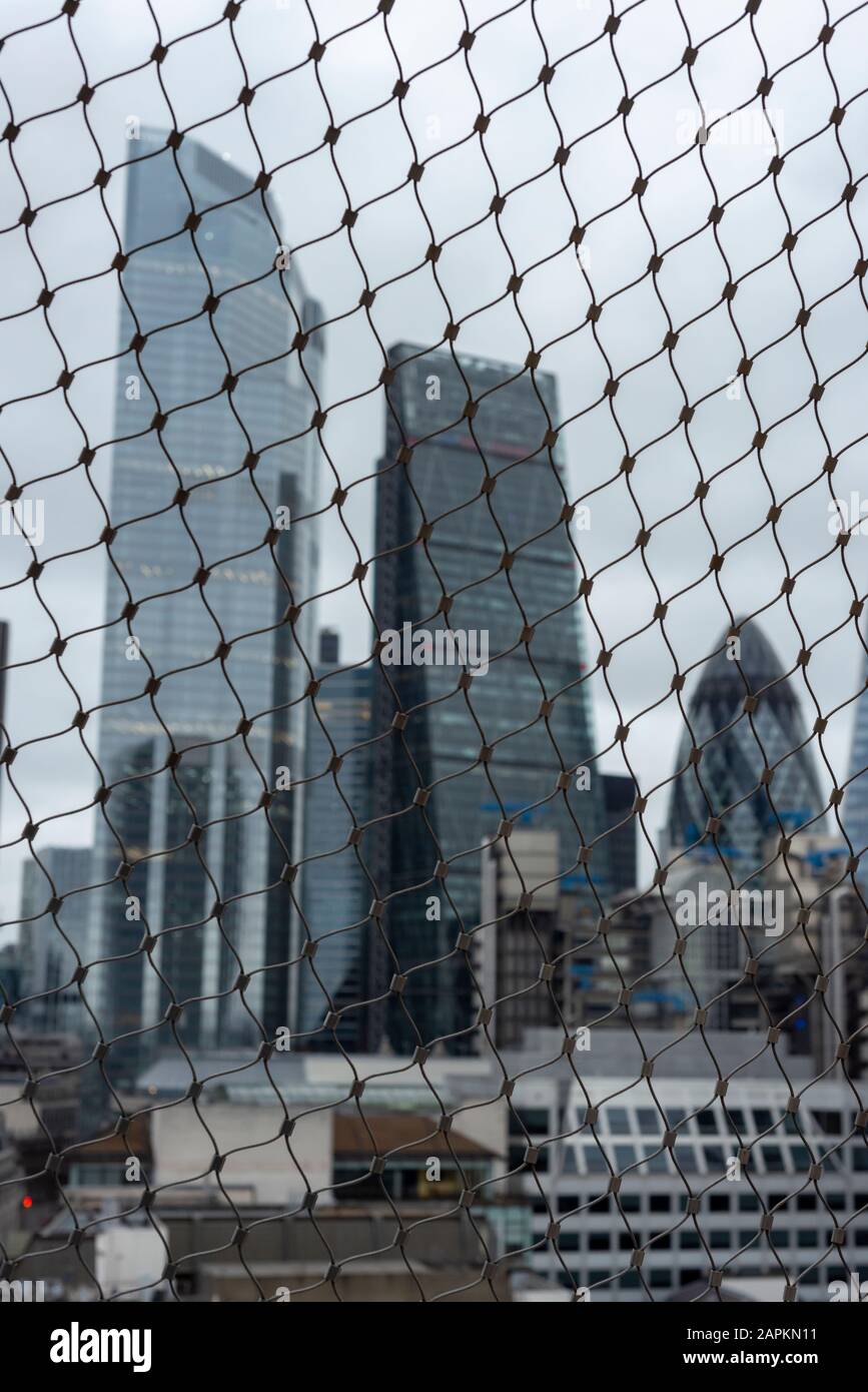 Ungewöhnlicher, entschärfener, behinderter Blick auf die Londoner City Gebäude durch Drahtgitterfechten von der Spitze des Monuments am trüben Tag in London Stockfoto