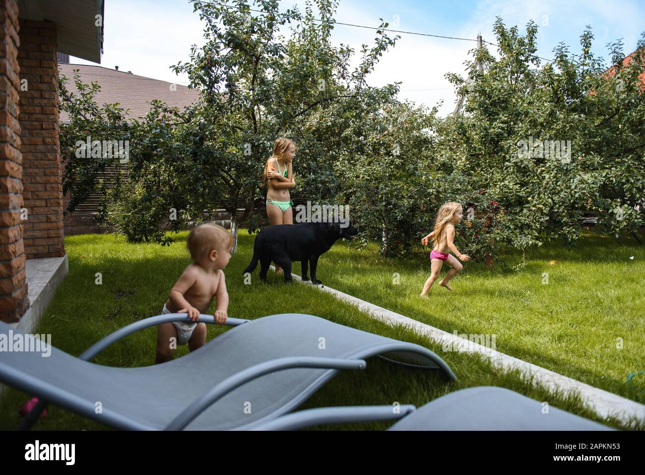 Kleines Mädchen, das mit Wasser im Hof eines Hauses mit einem schwarzen Hund spielt Stockfoto