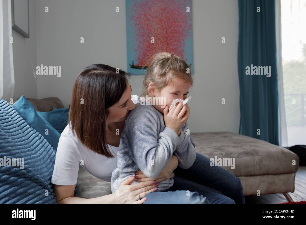 Mutter sitzt mit Tochter, die ihre Nase auf der Couch im Wohnzimmer zuhause weht Stockfoto