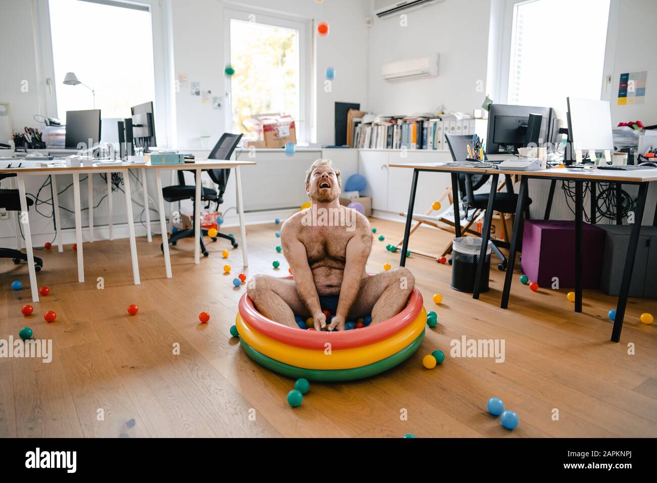 Verrückter Geschäftsmann, der im Planschbecken im Büro sitzt und mit Bällen spielt Stockfoto