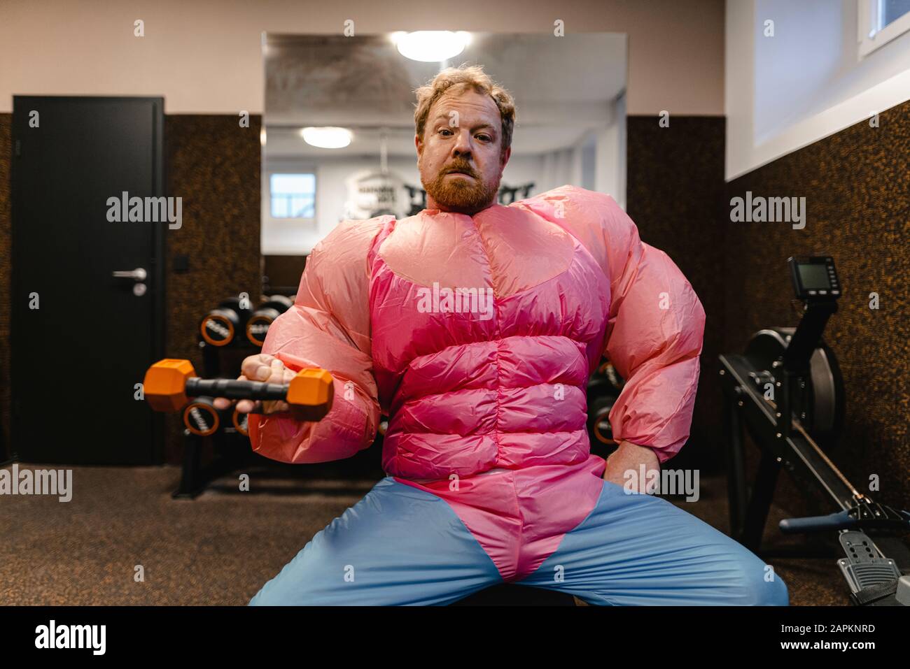 Mann im Fitnessstudio mit pinkfarbenem Body Builder Kostüm mit Hanteln Stockfoto