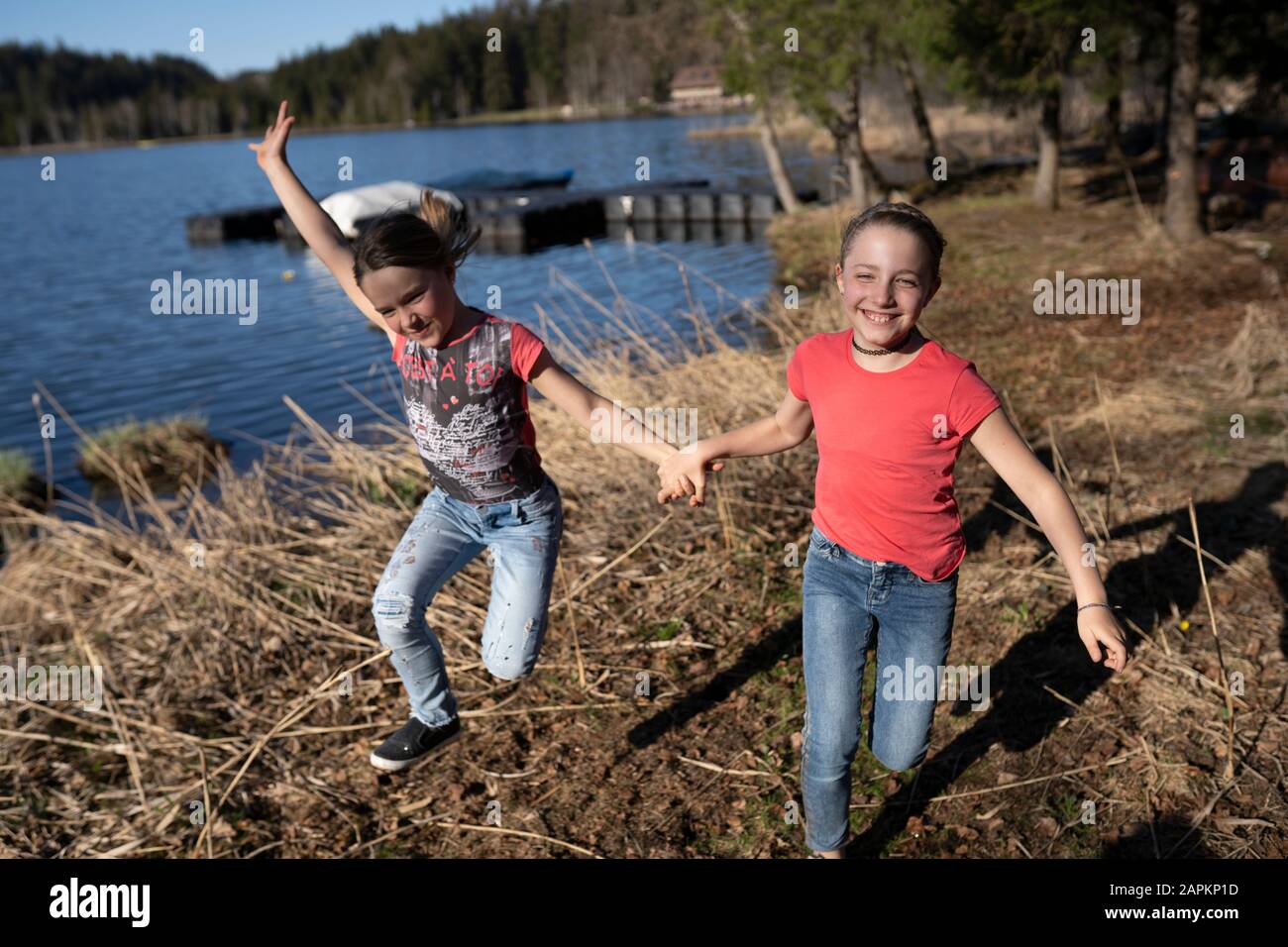 Schwestern, die Spaß am See haben, Hand halten, laufen und springen Stockfoto