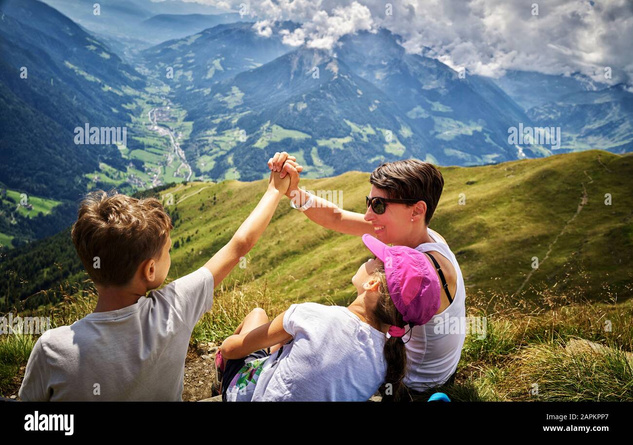 Glückliche Mutter mit zwei Kindern, die eine Pause vom Wandern in der Alpenlandschaft, Passeiertal, Südtirol, Italien, einlegen Stockfoto