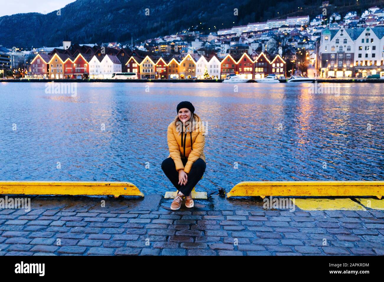 Frau, die eine gelbe Jacke trägt und am Hafen in Bergen, Norwegen sitzt Stockfoto