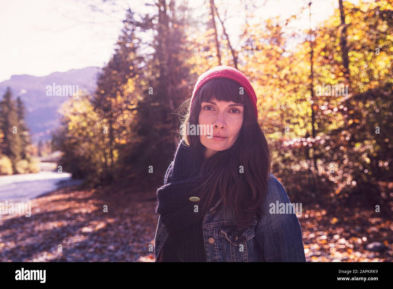 Frau, die im Herbst roten wolligen Hut und Denimjacke am Flussufer trägt Stockfoto