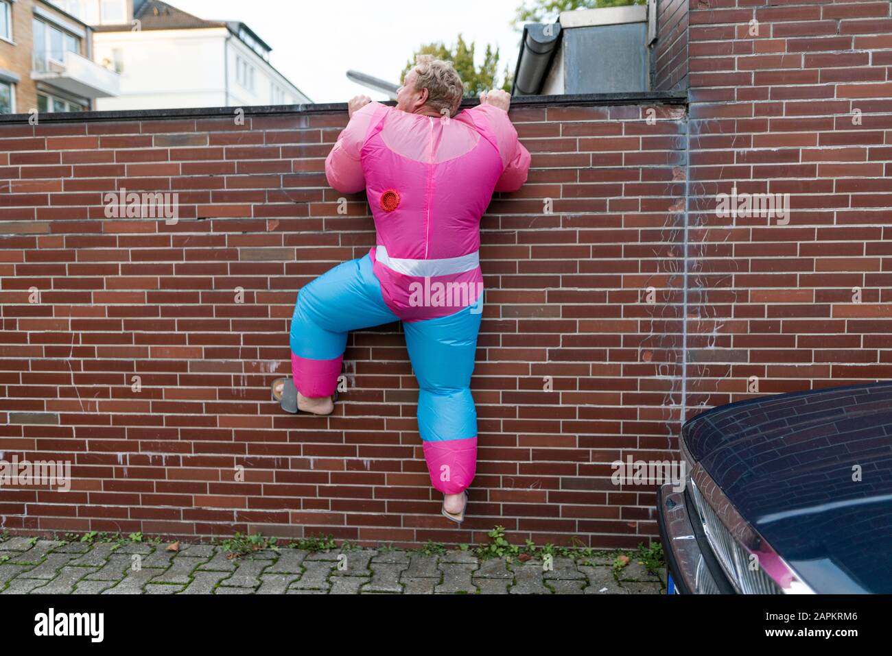 Mann mit rosafarbenem Bodybuilder-Kostüm, der über eine Wand klettert Stockfoto