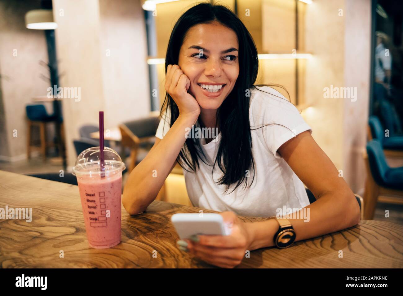 Schwarz-haarige Frau trinkt einen Smoothie und benutzt Smartphone im Café Stockfoto