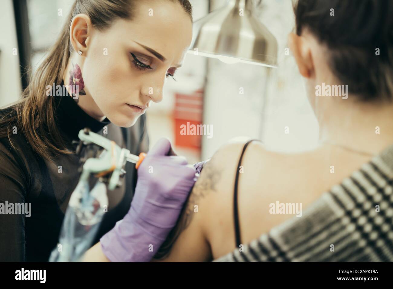 Tätooistische Frauen, die den Oberarm der weiblichen Kundin tätowieren Stockfoto