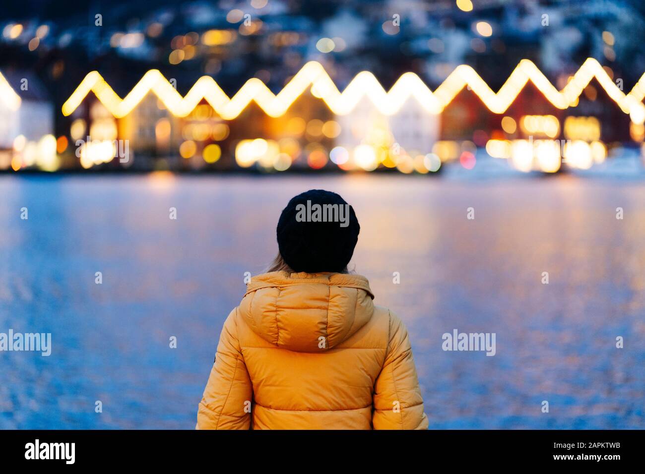 Rückansicht der Frau, die eine gelbe Jacke trägt und am Hafen in Bergen, Norwegen steht Stockfoto