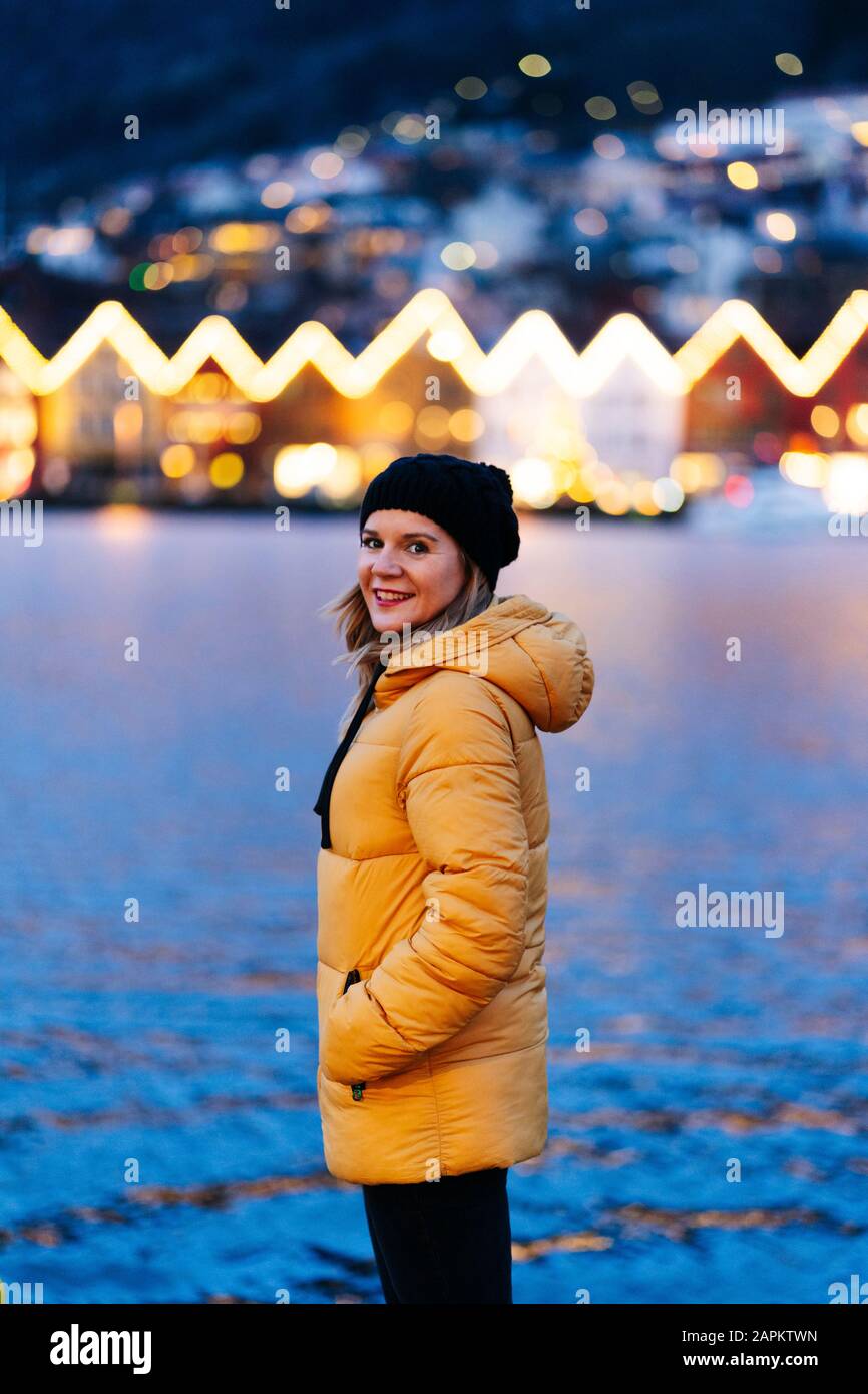 Frau, die eine gelbe Jacke trägt und am Hafen in Bergen, Norwegen sitzt Stockfoto