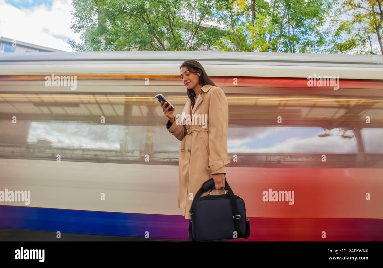 Junge Geschäftsfrau mit Smartphone vor dem Pendlerzug Stockfoto