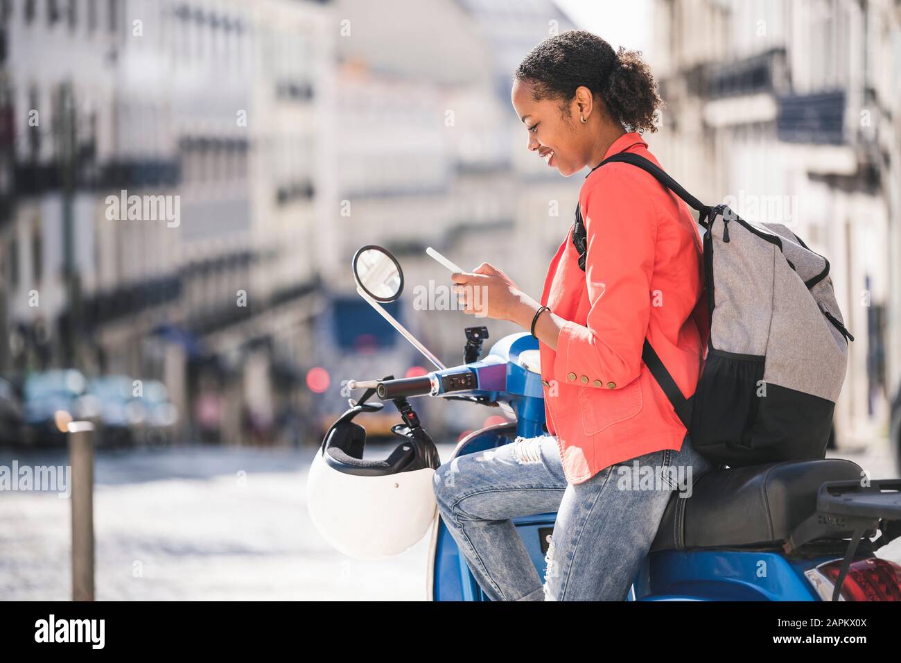 Junge Frau mit Handy auf Motorroller in der Stadt Lissabon, Portugal Stockfoto