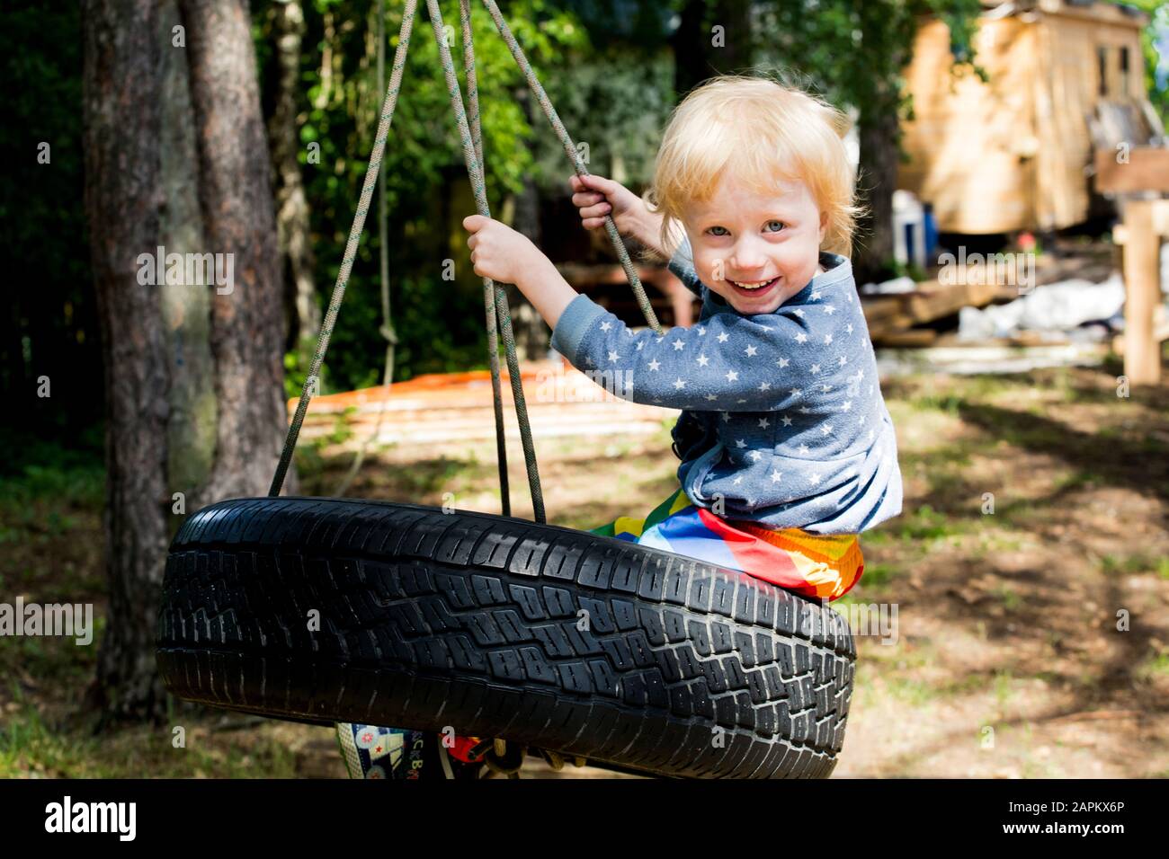 Porträt eines glücklichen Kleinkindmädchens, das auf Reifenschwinge sitzt Stockfoto