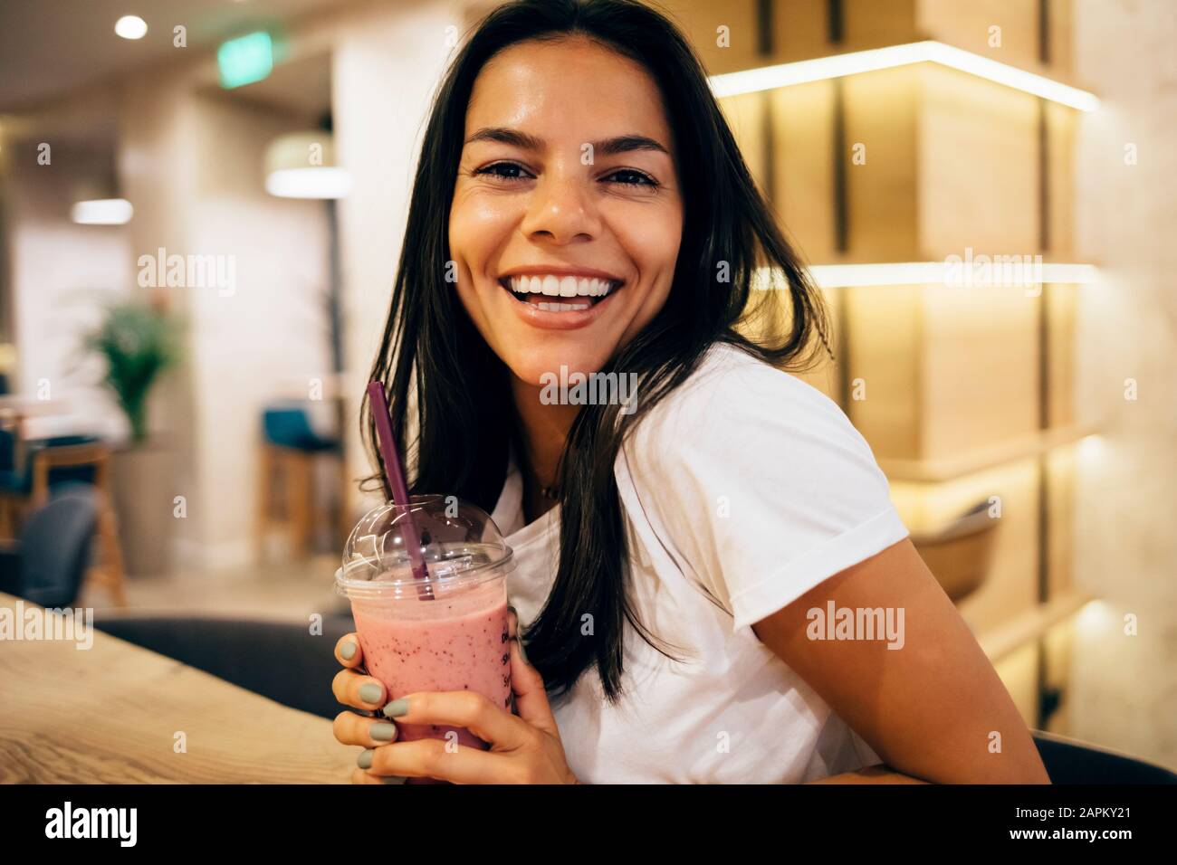 Schwarz-haarige Frau trinkt im Café einen Smoothie Stockfoto