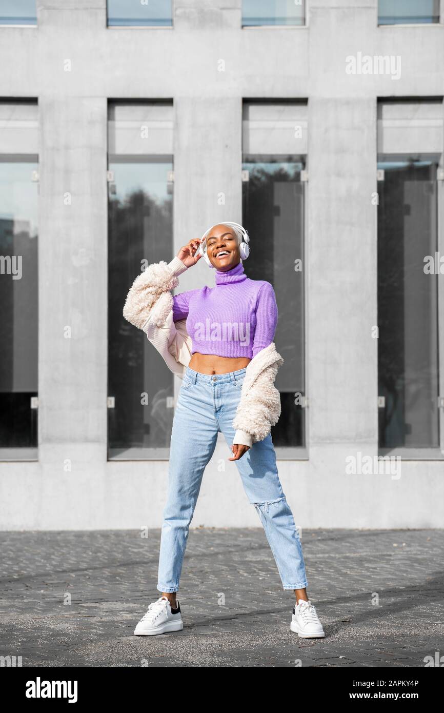Weiße, haarige Frau mit weißen Kopfhörern, die Musik hören und in der Stadt tanzen Stockfoto