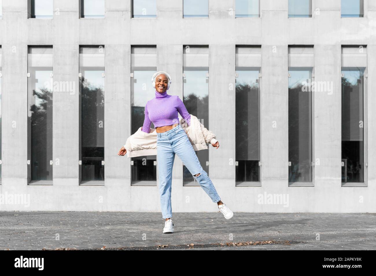 Weiße, haarige Frau mit weißen Kopfhörern, die Musik hören und in der Stadt tanzen Stockfoto