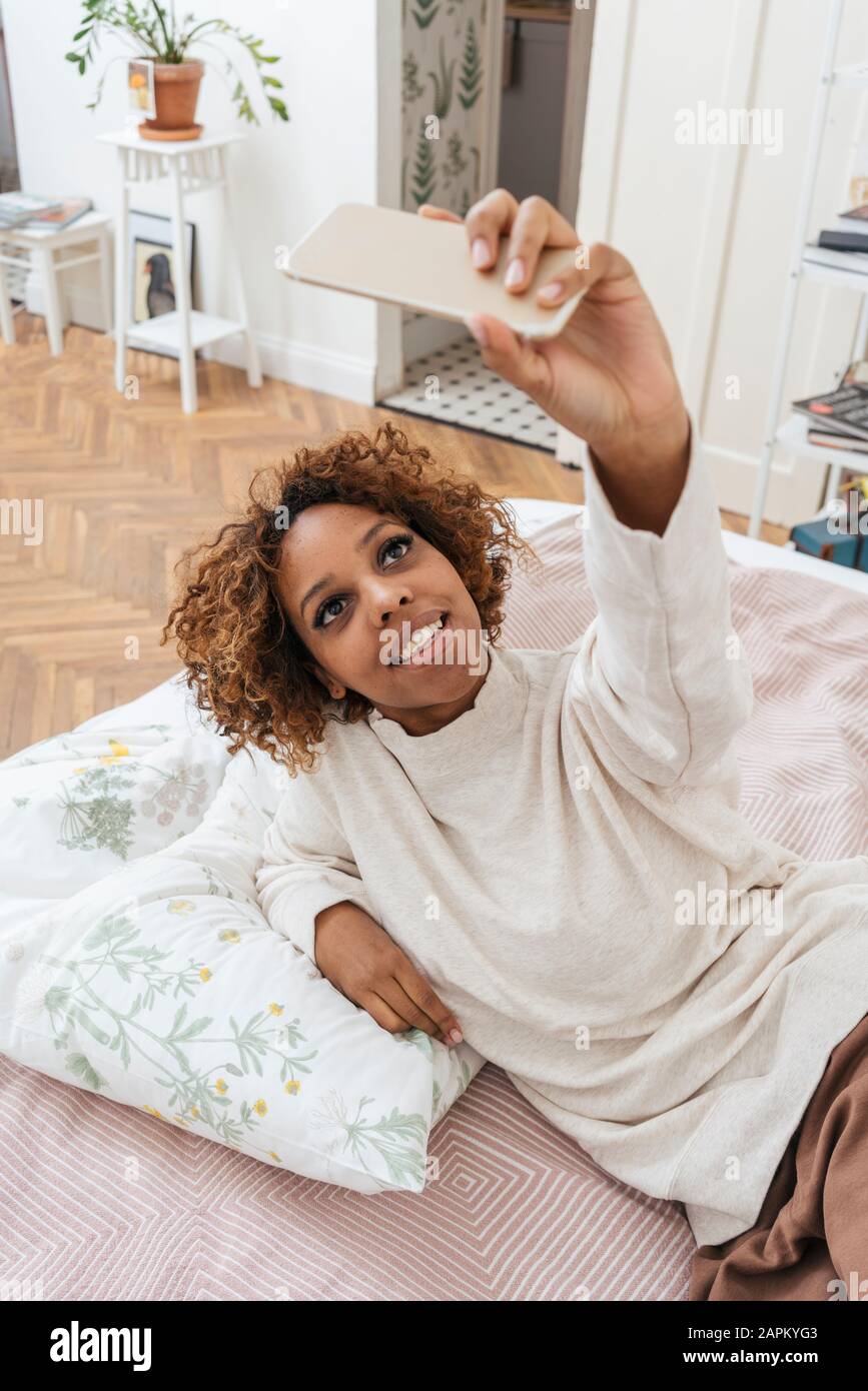 Glückliche junge Frau, die im Bett liegt und eine selfie nimmt Stockfoto