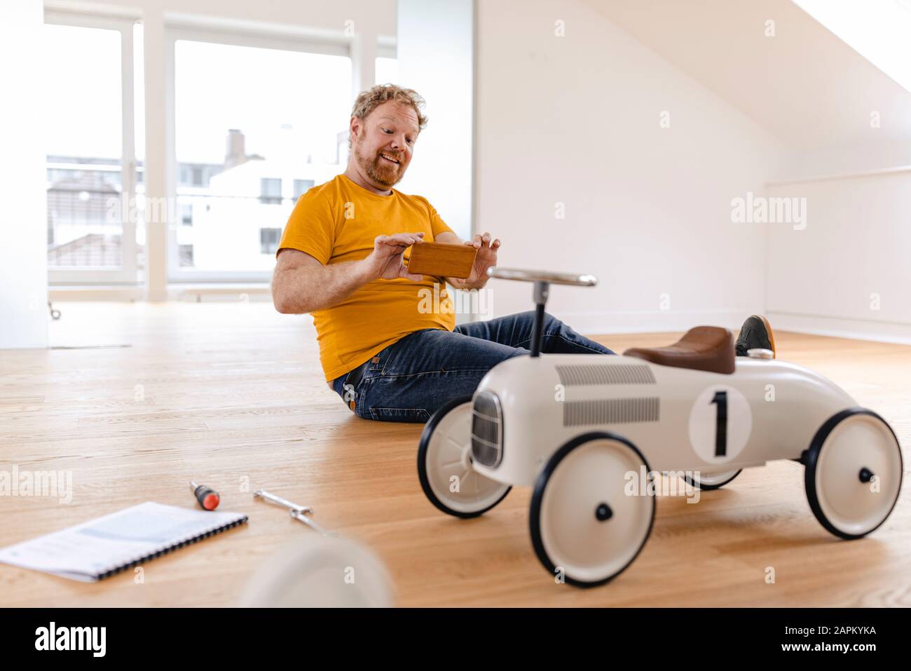 Glücklicher Mann nimmt Handyfoto von Spielzeugauto auf Stockfoto