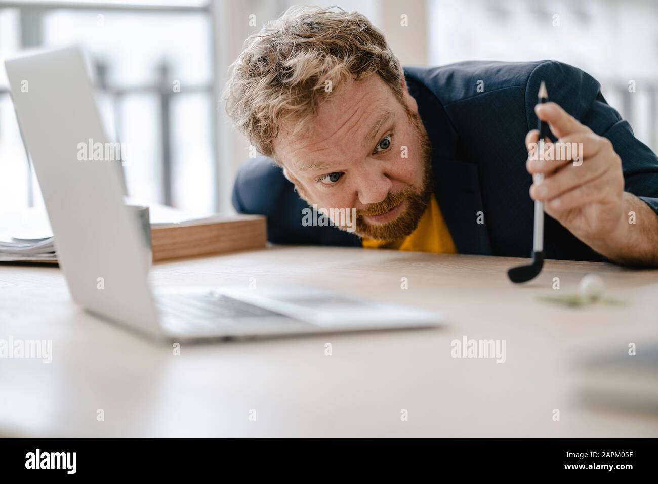 Geschäftsmann, der auf dem Schreibtisch im Büro Golf spielt Stockfoto