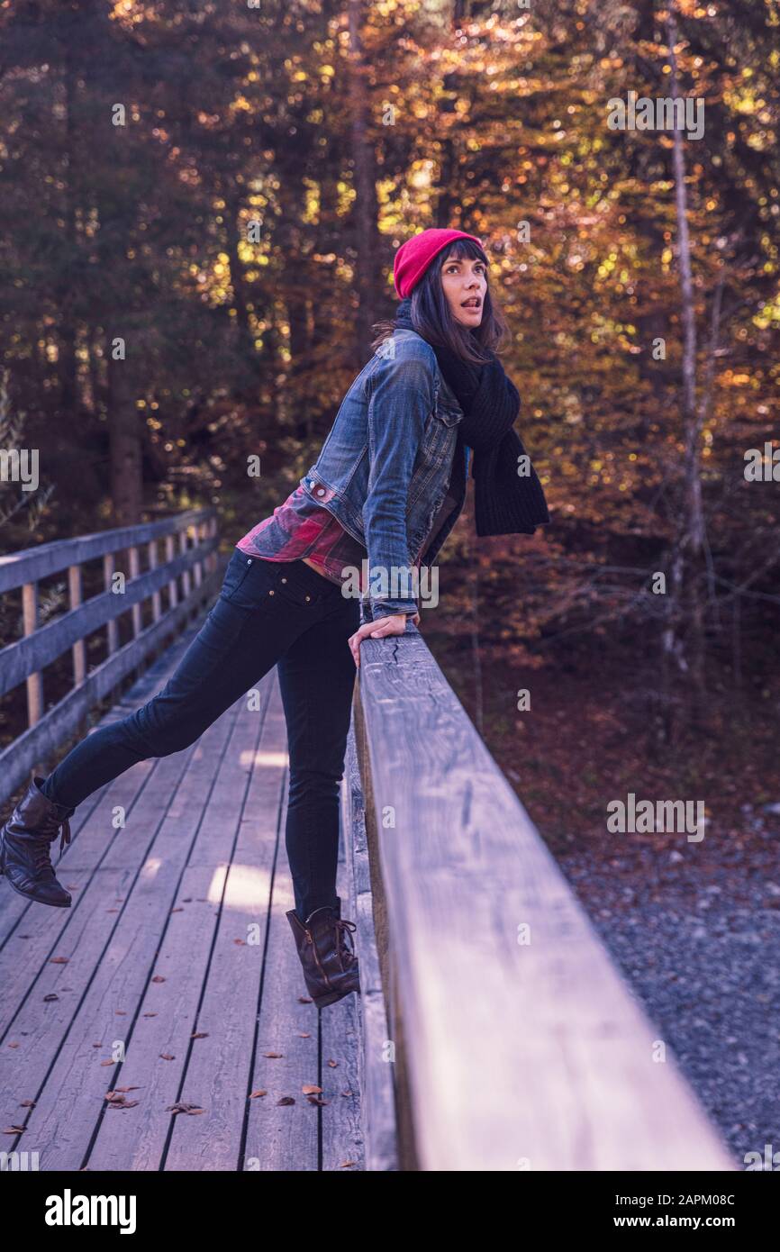 Frau trägt im Herbst roten wolligen Hut und Denimjacke auf einer Brücke Stockfoto
